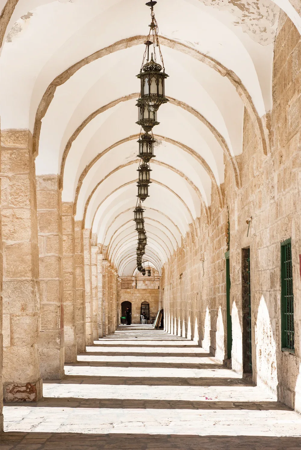 A long stone colonnade with hanging lanterns, its arches receding in a straight line